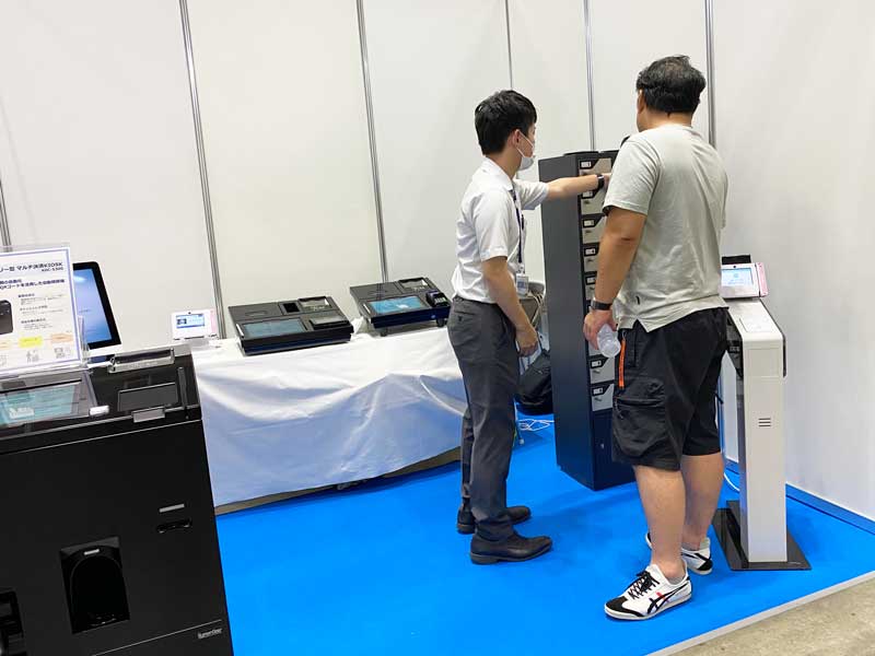 セキュリティー対策としてICカードと暗証番号のダブルセキュリティで開閉できる貴重品ボックスや、IC付きの身分証（会員証、職員証、互助会員カードなど）のデータ収集に最適なマルチリーダー端末を説明している様子